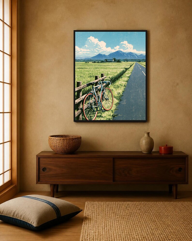 May include: A framed wall art print depicting a landscape scene with a bicycle leaning against a wooden fence beside a paved road. The image features a green field, distant blue mountains, and a bright blue sky with white clouds.