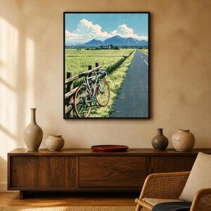 May include: A framed wall art print depicting a road bike leaning against a wooden fence beside a paved road. The scene features a green field, a distant mountain range under a blue sky with white clouds, and a textured, illustrated aesthetic.