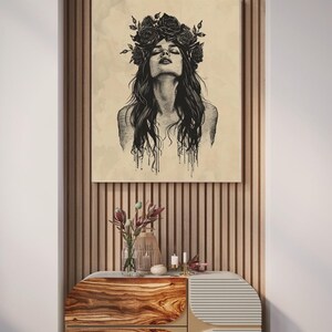 May include: A rectangular wall art print featuring a black ink illustration of a person with long hair and a floral crown, set against a light beige background. The artwork displays fine line work and dripping ink details on the lower edges.