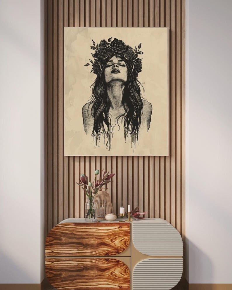 May include: A rectangular wall art print featuring a black ink illustration of a person with long hair and a floral crown, set against a light beige background. The artwork displays fine line work and dripping ink details on the lower edges.