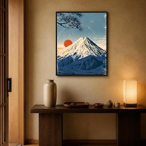 May include: A framed wall art print depicting a snow-capped mountain peak under a blue sky with a prominent red sun and pine tree branches. The artwork features a textured, vintage-inspired aesthetic with deep blue, white, and orange colour tones.