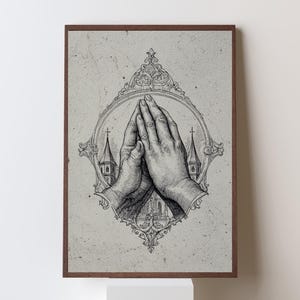 Op de afbeelding: Een ingelijste kunstdruk met een zwart-witte inktillustratie van twee handen die in gebed zijn samengevouwen. De handen zijn gecentreerd in een sierlijke, ovale lijst, met de silhouetten van twee kerktorens zichtbaar op de achtergrond.