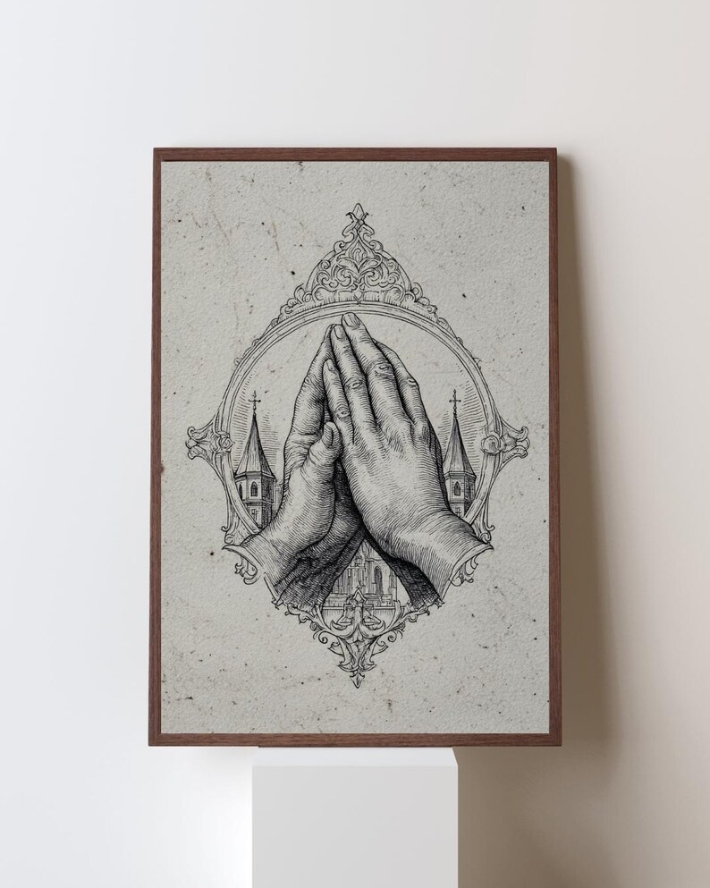 Op de afbeelding: Een ingelijste kunstdruk met een zwart-witte inktillustratie van twee handen die in gebed zijn samengevouwen. De handen zijn gecentreerd in een sierlijke, ovale lijst, met de silhouetten van twee kerktorens zichtbaar op de achtergrond.