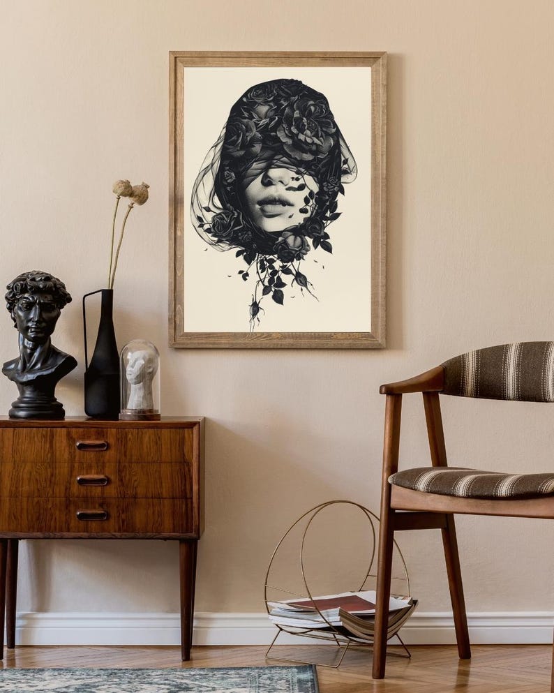 Op de afbeelding: Een ingelijste kunstdruk met een zwart-witillustratie van een gezicht dat gedeeltelijk wordt bedekt door een sluier van donkere rozen en bladeren. Het kunstwerk zit in een lichtgekleurde houten lijst en toont gedetailleerde florale vormen.