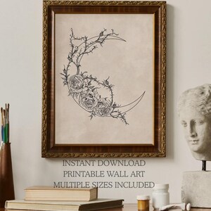 May include: A framed wall art print featuring a black line drawing of a crescent moon adorned with roses and thorny vines on a beige background. The text below reads INSTANT DOWNLOAD PRINTABLE WALL ART MULTIPLE SIZES INCLUDED in dark gray lettering.