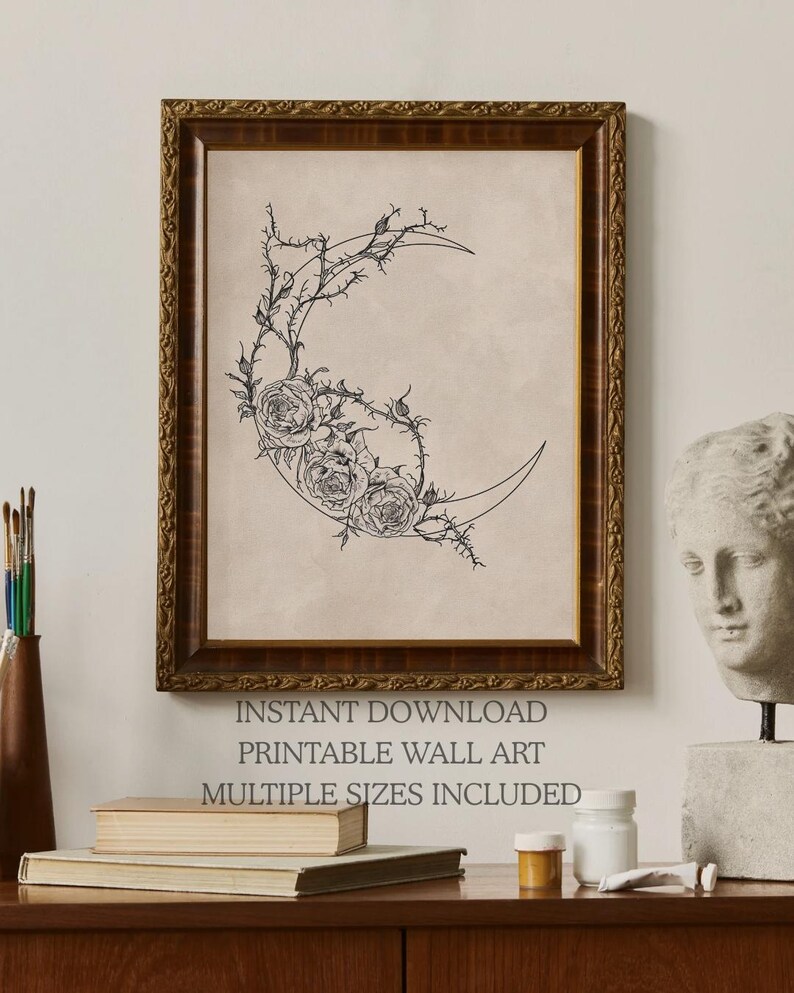 May include: A framed wall art print featuring a black line drawing of a crescent moon adorned with roses and thorny vines on a beige background. The text below reads INSTANT DOWNLOAD PRINTABLE WALL ART MULTIPLE SIZES INCLUDED in dark gray lettering.