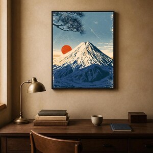 May include: A framed wall art print featuring a stylised illustration of a snow-capped mountain peak under a blue sky with a prominent red sun and a pine tree branch in the upper left corner, rendered in a textured, vintage-inspired graphic style.