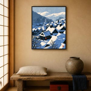 May include: A framed art print depicting a snowy village scene with dark houses featuring steep roofs covered in thick white snow, smoke rising from a chimney, and distant blue mountains under a clear sky, rendered in a stylized graphic art style.