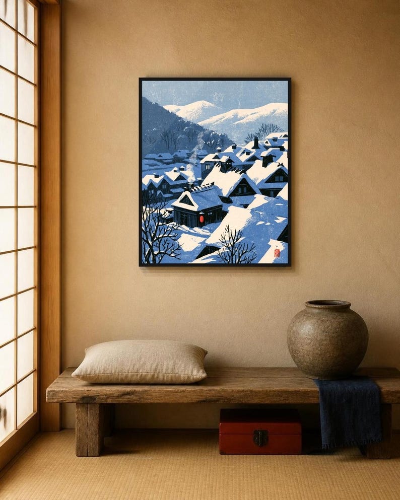 May include: A framed art print depicting a snowy village scene with dark houses featuring steep roofs covered in thick white snow, smoke rising from a chimney, and distant blue mountains under a clear sky, rendered in a stylized graphic art style.