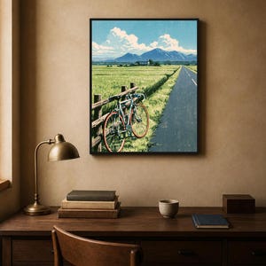 May include: A framed wall art print depicting a light blue bicycle with red wheels leaning against a wooden fence beside a paved road. The scene features a vast green field, distant mountains, and a blue sky with white clouds in a landscape orientation.