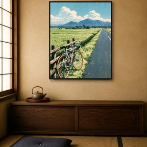 May include: A framed wall art print depicting a light blue road bicycle leaning against a wooden fence beside a paved road. The scene features a vast green field, distant mountains, and a bright blue sky with white clouds in a landscape orientation.
