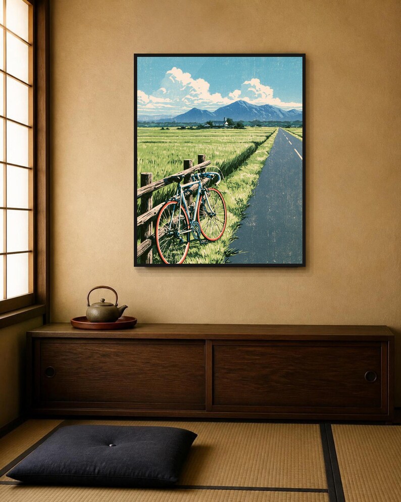 May include: A framed wall art print depicting a light blue road bicycle leaning against a wooden fence beside a paved road. The scene features a vast green field, distant mountains, and a bright blue sky with white clouds in a landscape orientation.