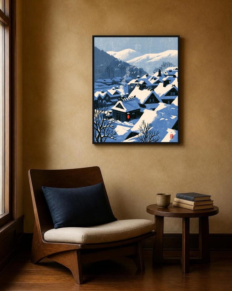 May include: A framed wall art print depicting a snow-covered village nestled in a valley with mountains in the background. The scene features dark-roofed houses with white snow, a single red lantern, and a small red seal in the bottom corner.