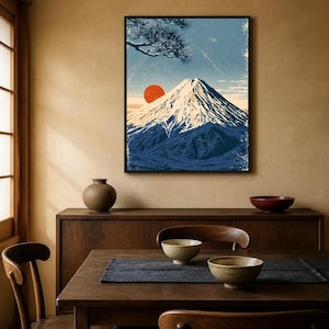 May include: A framed wall art print featuring a stylised illustration of Mount Fuji with a snow-capped peak, a vibrant orange sun, and dark blue pine tree branches in the upper corner, set against a textured light blue sky background.