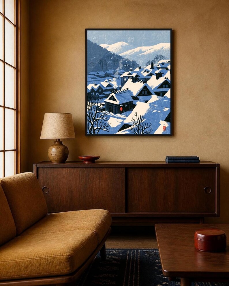 May include: A framed wall art print depicting a snowy Japanese village scene with traditional gabled houses covered in deep snow, blue shadows, and distant mountains under a pale sky, featuring a small red circular seal in the bottom right corner.