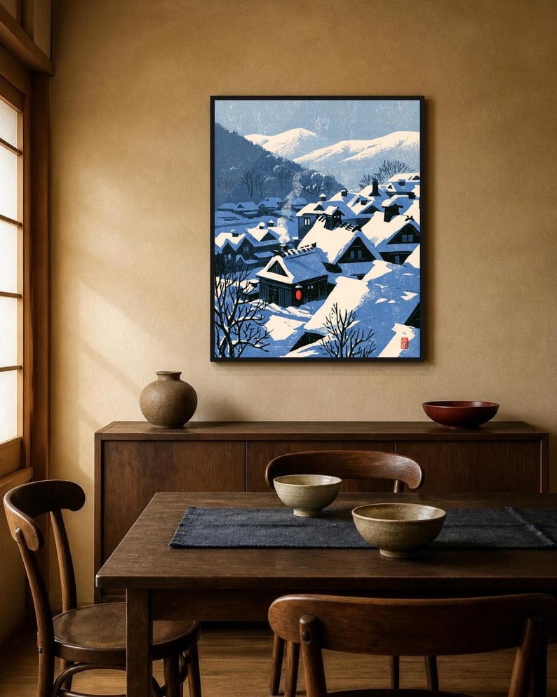 May include: A framed wall art print depicting a snowy village scene with dark-roofed houses covered in thick white snow, bare trees, and distant mountains under a pale blue sky. A single red lantern glows near a house, and a small red seal is visible.
