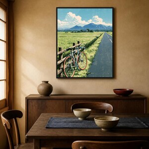 May include: A framed wall art print depicting a landscape with a road, a green field, and a bicycle leaning against a wooden fence. The scene features distant blue mountains under a bright blue sky with white clouds, rendered in a graphic style.
