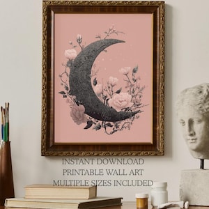 May include: A framed wall art print featuring a dark, textured crescent moon surrounded by light pink flowers and vines against a solid dusty pink background. The text below the frame reads: INSTANT DOWNLOAD PRINTABLE WALL ART MULTIPLE SIZES INCLUDED.