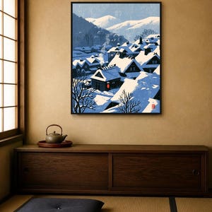 May include: A framed wall art print depicting a snowy Japanese village scene with traditional houses featuring steep, snow-covered roofs, smoke rising from chimneys, and distant mountains under a pale blue sky, with a small red lantern accent.