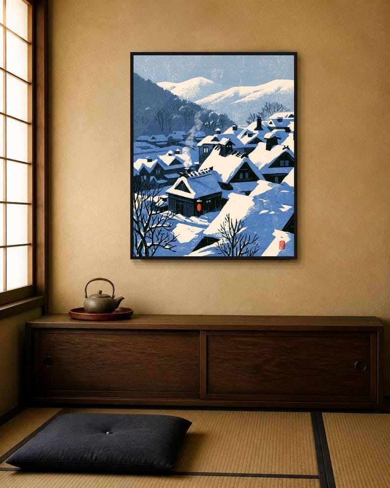 May include: A framed wall art print depicting a snowy Japanese village scene with traditional houses featuring steep, snow-covered roofs, smoke rising from chimneys, and distant mountains under a pale blue sky, with a small red lantern accent.