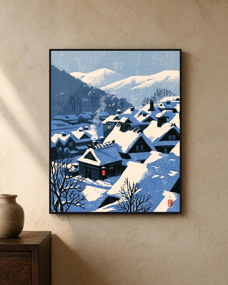 May include: A framed art print depicting a snowy village scene with dark wooden houses, deep blue shadows, and white snow-covered roofs. A single red lantern glows near a house, while smoke rises into a pale blue sky against distant mountains.