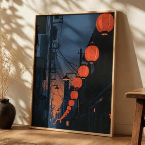 May include: A framed vertical wall art print depicting a narrow street scene at dusk, featuring a long string of glowing orange paper lanterns hanging above a dark alleyway with utility poles, wires, and silhouettes of buildings.