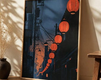 May include: A framed vertical wall art print depicting a narrow street scene at dusk, featuring a long string of glowing orange paper lanterns hanging above a dark alleyway with utility poles, wires, and silhouettes of buildings.
