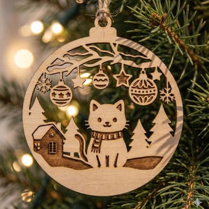 Pode incluir: Enfeite de Natal de madeira redondo com um gato com cachecol, uma casa e árvores. O enfeite tem desenhos recortados de flocos de neve, estrelas e bolas de Natal. Pendurado em um fio de barbante natural.