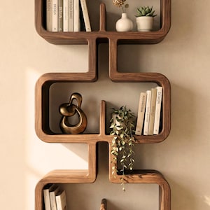 Puede incluir: Un estante de pared de madera moderno con un diseño curvo único. Los estantes exhiben libros, pequeñas plantas y objetos decorativos, incluyendo una escultura dorada y un cuenco pequeño. La unidad es de madera oscura y está montada en una pared de color neutro.