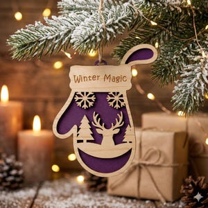 Op de afbeelding: Houten wantvormige kerstversiering met de tekst "Winter Magic". De versiering heeft een paars interieur met uitgesneden sneeuwvlokken, bomen en een hert. Het hangt aan een besneeuwde dennentak, met brandende kaarsen en ingepakte cadeaus op de achtergrond.