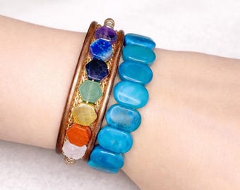 May include: Two bracelets on a wrist. One is a brown leather cuff with seven colorful gemstone accents. The other is a turquoise beaded bracelet. The gemstones are purple, blue, green, yellow, orange, and pink.