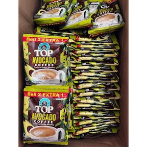 Puede incluir: Una caja llena de numerosos paquetes de café Top Avocado. Los paquetes son principalmente verdes, marrones y amarillos, con el nombre de la marca y una imagen de taza de café. El texto "Beli 2 EXTRA 1" también es visible.