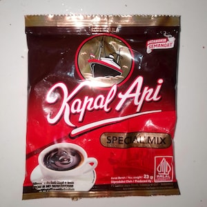 May include: A rectangular brown and red coffee packet labeled Kapal Api Special Mix. The packaging features a graphic of a ship, a white cup of black coffee on a saucer, and text including Net Weight 23 g and a Halal certification logo.
