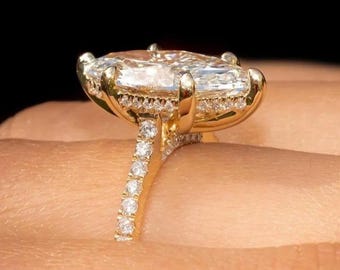 May include: A gold ring with a large, rectangular, clear gemstone as the centerpiece. The ring's band and the setting around the main stone are encrusted with smaller, clear gemstones. The ring is held by a person. The text "ROSSY JewelsIN" is in the upper right corner.