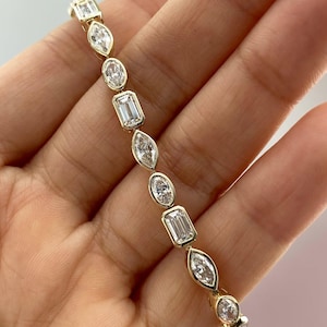 Könnte beinhalten: Ein goldenes Armband mit Diamanten in verschiedenen Formen, darunter oval, Smaragd- und Marquise-Schliff. Die Diamanten sind in einzelnen Goldfassungen gefasst. Das Armband wird vor einem neutralen Hintergrund gezeigt. Länge ca. 18 cm.