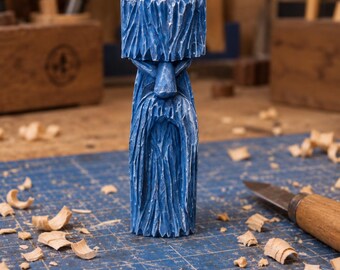 May include: A hand-carved wooden figurine of a bearded figure with a prominent hat, finished in a vibrant blue paint. The sculpture features deep, textured chisel marks throughout the surface, depicting a long beard and facial features.