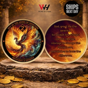 May include: Two gold-coloured recovery coins. One coin features a phoenix rising from flames, with the text "OUT OF THE ASHES OF ADDICTION" and "RECOVERY & GROWTH". The other coin has the Serenity Prayer.