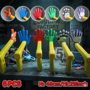 May include: Six colorful toy hand grabbers with yellow arms, each with a different hand color: orange, blue, red, green, white, and purple. The height is 19.29 inches. The text "Playtime Co. Factory" is visible in the background.