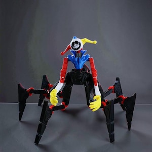 May include: A colorful toy robot in the shape of a spider with a jester's head. The robot has a blue, red, yellow, black, and white color scheme. The legs are black with red joints, and the head features a smiling face.