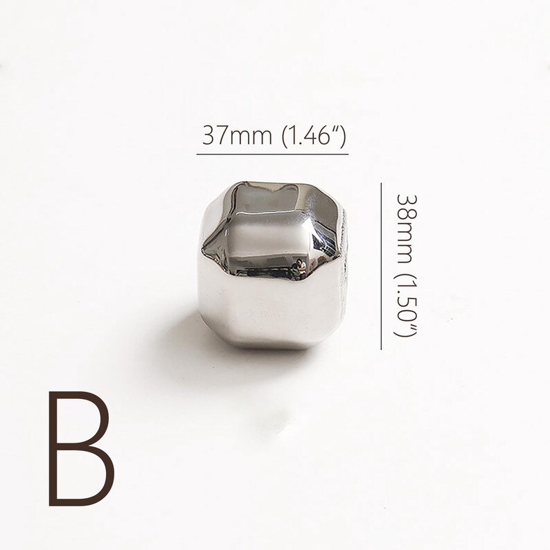 Op de afbeelding: Een glanzende, zilverkleurige, geometrische kraal, 37mm breed en 38mm hoog. De letter "B" staat in de linker benedenhoek. De kraal heeft een reflecterend oppervlak en een unieke, facetvorm. Ideaal voor het maken van sieraden.