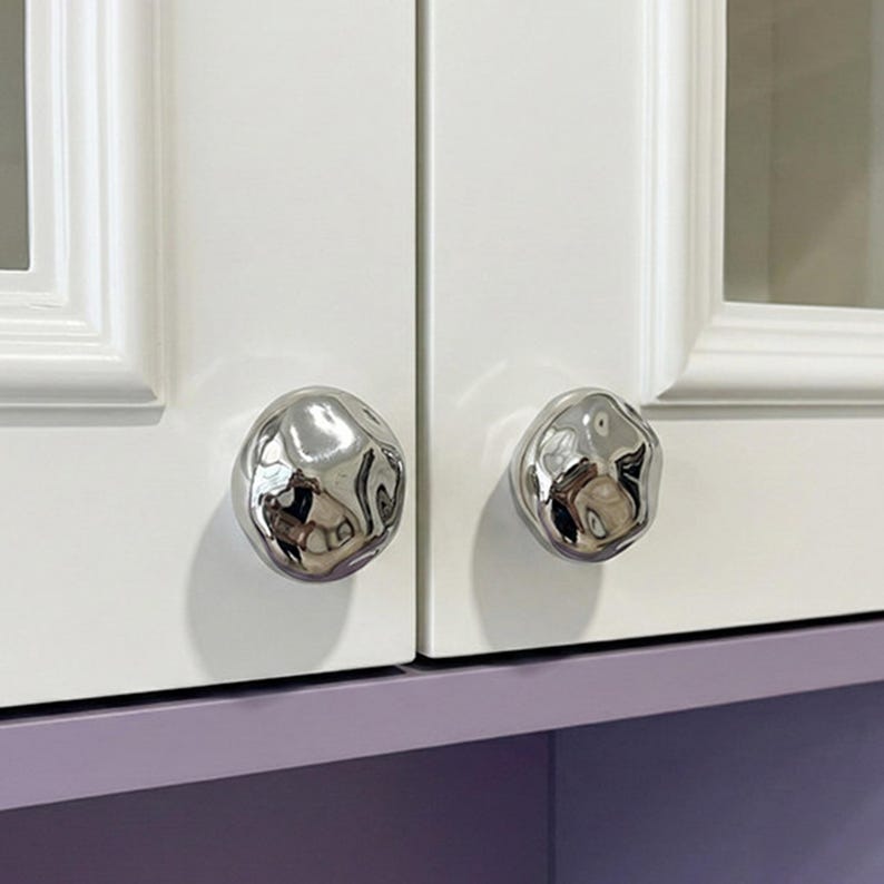 May include: A white ceramic mug with a black handle and the text "But First, Coffee" in a handwritten style. The mug is on a white surface. The mug is approximately 10 cm tall.