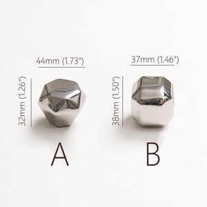 Op de afbeelding: Twee zilverkleurige, facetgeslepen decoratieve knoppen. Knop A meet 44 mm x 32 mm en knop B meet 37 mm x 38 mm. De knoppen zijn gelabeld met A en B.