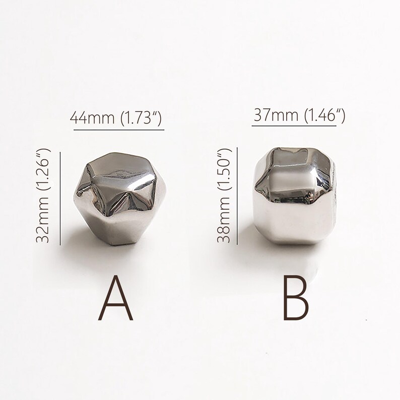 Op de afbeelding: Twee zilverkleurige, facetgeslepen decoratieve knoppen. Knop A meet 44 mm x 32 mm en knop B meet 37 mm x 38 mm. De knoppen zijn gelabeld met A en B.