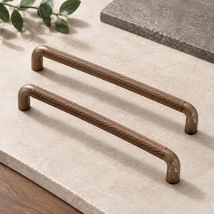 May include: Two bronze-toned metal cabinet pulls featuring a cylindrical bar design with a textured, cross-hatched knurled pattern across the center section and smooth, curved ends that attach to the mounting points for installation.