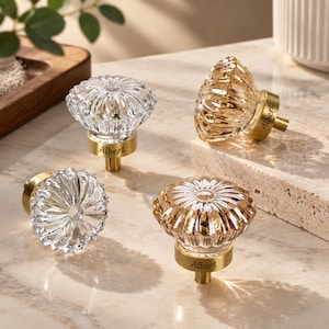 Puede incluir: Cuatro pomos redondos para armarios con tapas de cristal transparente facetado y bases de metal dorado. Cada base está grabada con el nombre Albert. Los pomos presentan un patrón radial en forma de flor sobre el cristal que refleja la luz.