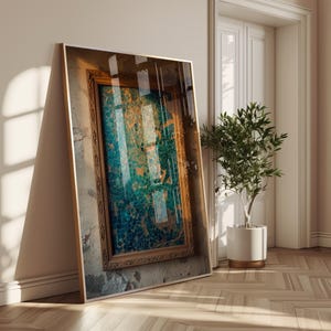 Op de afbeelding: Een ingelijst kunstwerk met een goudkleurige, sierlijke lijst. Het kunstwerk heeft een mozaïekachtig ontwerp in tinten van teal, blauw en goud. Het kunstwerk leunt tegen een muur met een baksteenstructuur, naast een witte deur en een potplant.