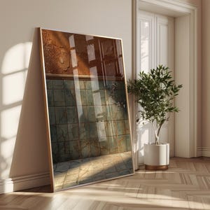 Könnte beinhalten: Ein gerahmter Kunstdruck, der an einer Wand lehnt. Das Kunstwerk zeigt ein strukturiertes, abstraktes Design mit Braun-, Grün- und Grautönen. Der Rahmen ist goldfarben, und der Druck wird in einem gut beleuchteten Raum mit einer Pflanze ausgestellt.