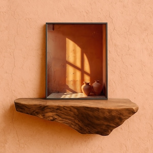Peut inclure: Une œuvre encadrée représentant un intérieur ensoleillé avec deux vases en terre cuite. L'œuvre repose sur une étagère en bois rustique contre un mur pêche texturé. La scène capture la chaleur de la lumière naturelle.