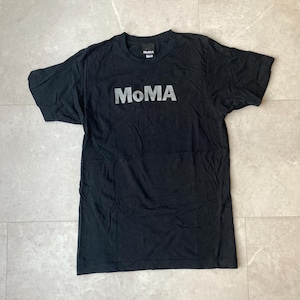 Può includere: T-shirt nero con la scritta "MoMA" in lettere argentate sul petto. La maglietta ha maniche corte e girocollo. Il logo MoMA è visibile anche sul retro del collo.