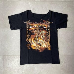 Op de afbeelding: Een zwart t-shirt met korte mouwen en een grafische print van een skelet op een paard. Het ontwerp bevat de tekst DragonForce in een gestileerd lettertype, omringd door sierlijke goud- en oranjekleurige randen met bliksemelementen.